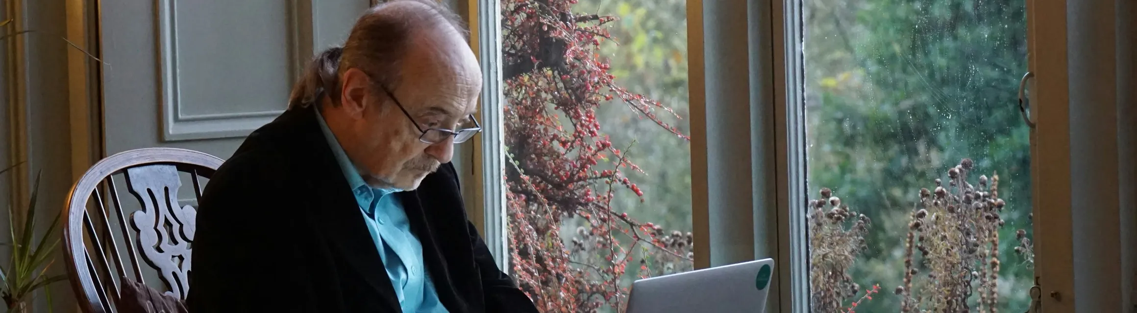 Un homme âgé à son portable près d'une fenêtre, feuillage d'automne à l'extérieur
