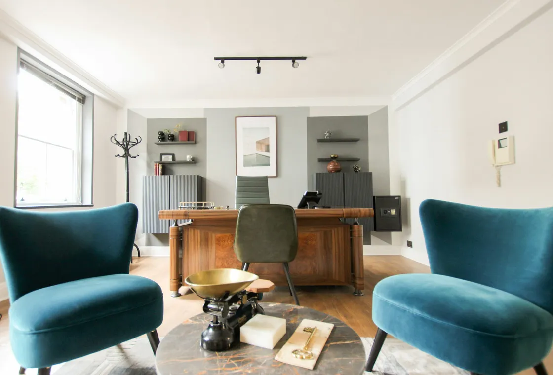 A bright consulting room with two armchairs and a desk by the window