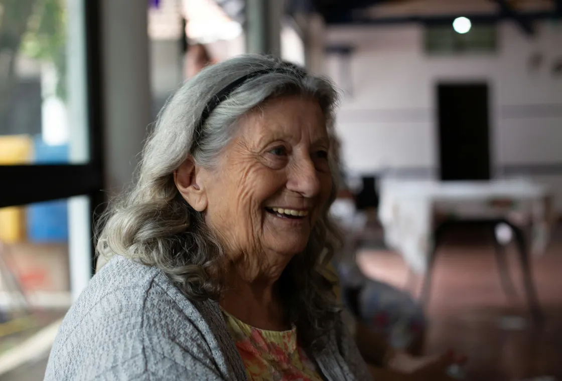 An older woman smiling, listening in a bright room
