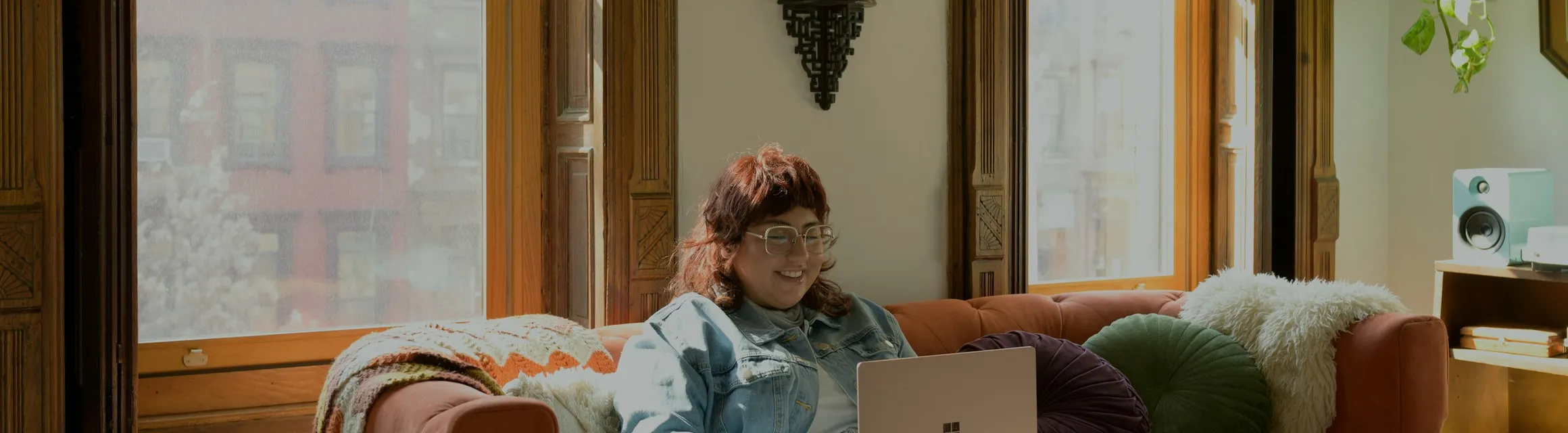 A woman on her sofa by a bright window, laptop open for a session