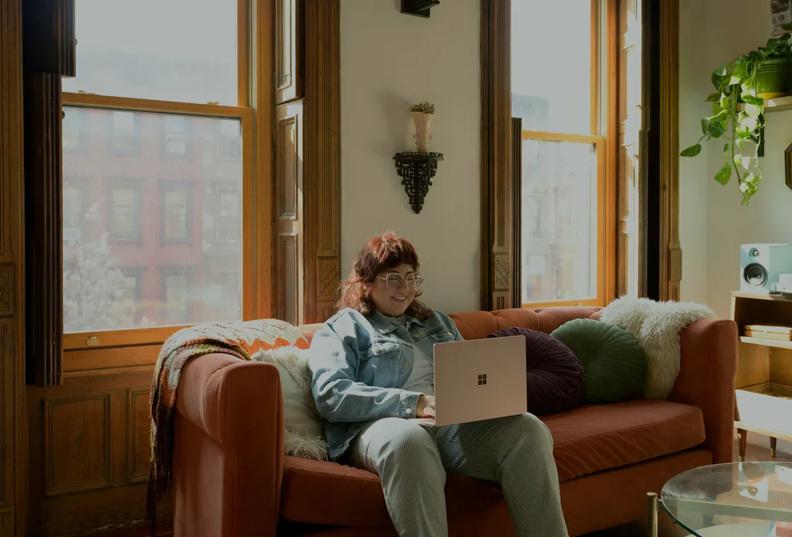A woman on her sofa by a bright window, laptop open for a session