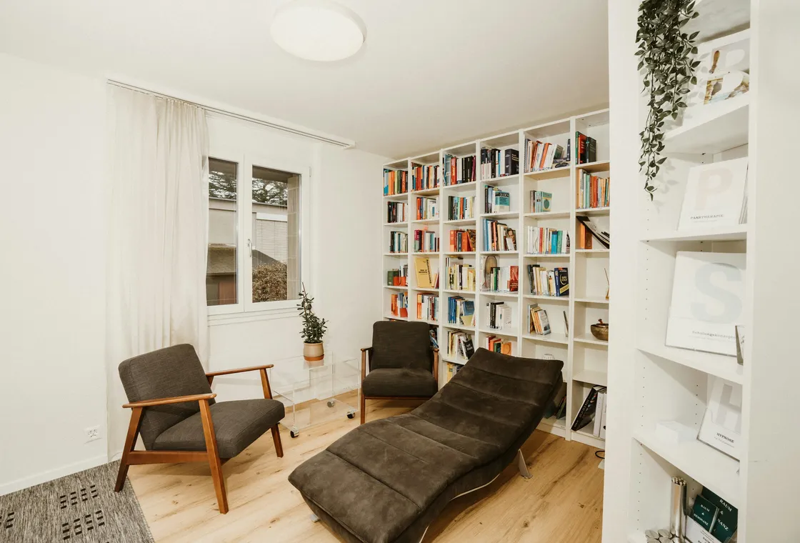 Une pièce calme avec un fauteuil, une méridienne et des rayonnages garnis
